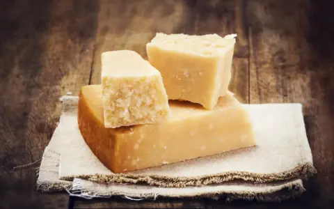 Drei Stücke Hartkäse, vielleicht Pecorino oder Parmesan, liegen auf einem Leinentuch vor rustikalem Holz.