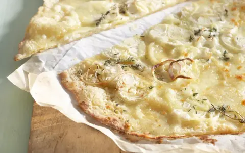 Dünne, knusprige knoblauch pizza mit geschmolzenem Käse und Zwiebelringen, garniert mit frischen Kräutern.