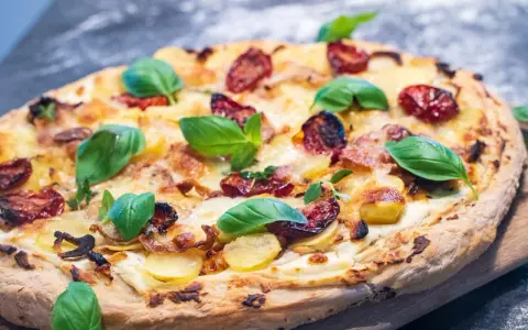 Pizza mit Sahne statt Tomatensauce, belegt mit Kartoffeln, getrockneten Tomaten und frischem Basilikum.