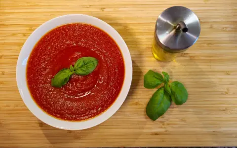 Schüssel mit cremiger Tomatensauce, garniert mit Basilikum. Daneben ein Glas Olivenöl und frische Basilikumblätter. Perfekt für Pasta mit San Marzano Tomaten.