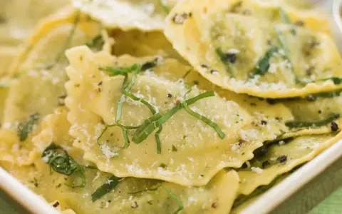 Mezzaluna pasta, gefüllt und mit Kräutern und Parmesan bestreut, liegt appetitlich in einer Schale.
