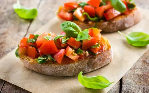 Zwei Bruschetta mit frischen Tomaten und Basilikum, warm oder kalt serviert, auf rustikalem Holztisch.