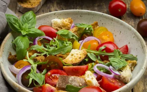Bunter Tomatensalat mit Brotstücken, Zwiebeln und Basilikum, verfeinert mit einem Hauch Balsamico Dressing.
