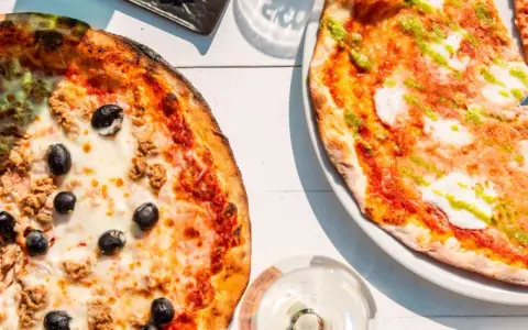 Zwei Pizzen, eine mit Thunfisch und Oliven, die andere mit Pesto. Das Geheimnis einer perfekten Pizza liegt oft im Mehl Typ 00.