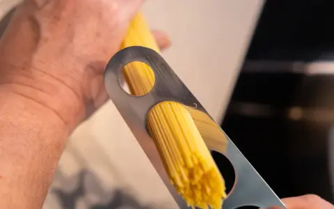 Ein Mann misst mit einem Metallwerkzeug die richtige Menge Spaghetti pro Person ab.