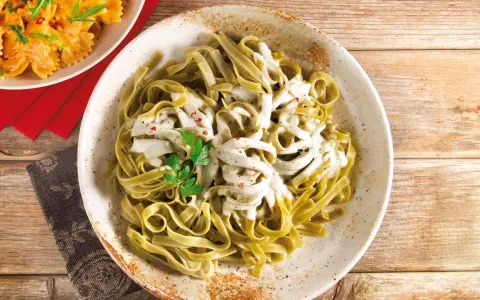 Grüne Bandnudeln mit cremiger Gorgonzola-Sauce, garniert mit Petersilie und roten Pfefferflocken.