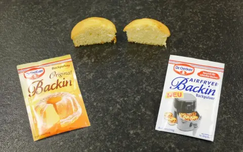 Zwei Päckchen Dr. Oetker Backin, einmal Original und einmal für den Airfryer, liegen neben zwei halbierten Küchlein. Perfekt für schnelles Backen mit Mehl und Backpulver.