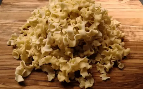 Ein Haufen ungekochte Pasta aus Hartweizengrieß (semola) liegt auf einem Holzbrett.