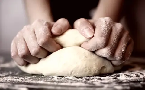 Hände kneten Teig, um die perfekte Konsistenz für Pizza zu erreichen. Die Frage "wie lange pizzateig kneten" beschäftigt viele Hobbybäcker.