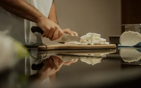 Hände schneiden Fior di Latte auf einem Holzbrett. Die frische Mozzarella-Masse wird für das Einfrieren vorbereitet.