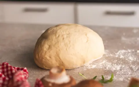 Frischer, goldgelber Pizzateig liegt bereit zum Formen. Ein paar Pilze und Rucola deuten auf eine leckere Pizza hin.