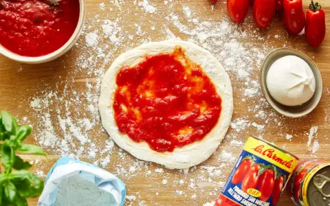 Pizza-Zutaten auf Holzbrett: Teig mit Tomatensauce, Mozzarella, frische Tomaten, Basilikum, Mehl und eine Dose San Marzano Tomaten. Die Frage "wieviel Tomatensauce pro Person" wird hier visuell beantwortet.