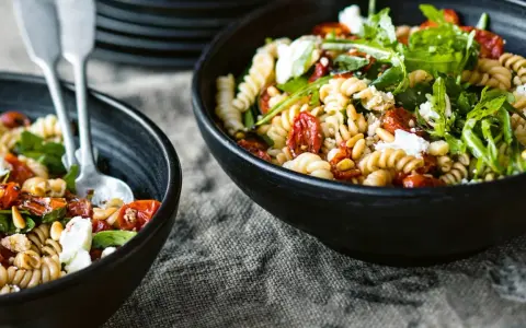 Zwei Schalen mit einem köstlichen nudelsalat mit getrockneten tomaten, Pinienkernen und Rucola.
