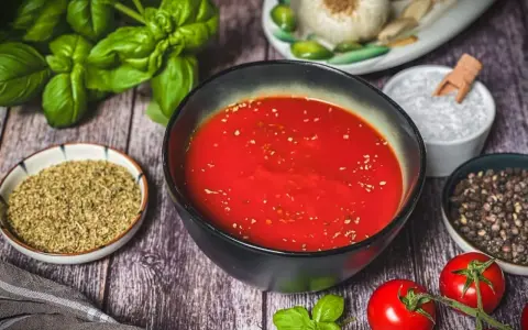Schüssel mit original italienischer pizzasauce, umgeben von frischem Basilikum, Tomaten, Knoblauch, Salz und Pfeffer.