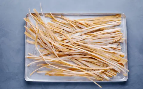 Frische, selbstgemachte Tagliatelle liegen auf einem Blech, bereit zum Kochen. Das Ergebnis von Tagliatelle selber machen.
