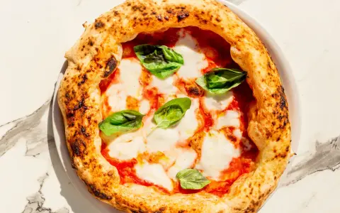 Eine klassische Pizza Napoli mit Tomaten, Mozzarella und frischem Basilikum. Der Belag ist einfach, aber perfekt für diese neapolitanische Spezialität.