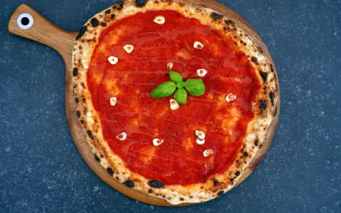 Eine köstliche Pizza Marinara mit Tomatensauce, Knoblauchscheiben und frischem Basilikum auf einem Holzbrett.