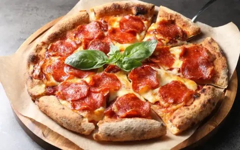 Eine köstliche Pizza mit geschmolzenem Käse und vielen Scheiben italienischer Salami, garniert mit frischem Basilikum.