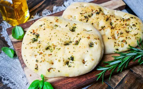 Zwei fluffige Pizzabrote mit Kräutern, perfekt gebacken mit Trockenhefe. Daneben frisches Basilikum und Rosmarin.