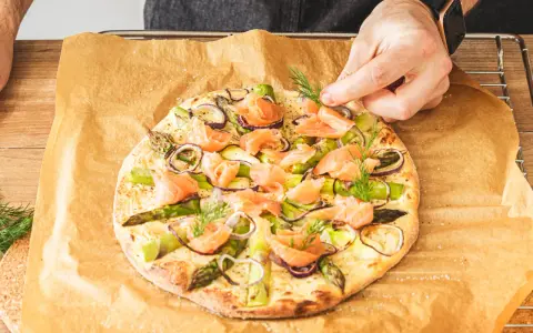 Eine köstliche Pizza mit Lachs, Spargel und roten Zwiebeln wird mit frischem Dill garniert.