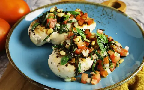 Zwei Hähnchenbrustfilets mit frischer Tomaten-Basilikum-Mischung und Pinienkernen, beträufelt mit Balsamico. Köstliche Bruschetta-Variante.