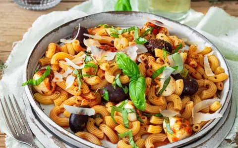 Ein köstlicher mediterraner Nudelsalat mit Pasta, Oliven, Mozzarella-Bällchen und frischem Basilikum, garniert mit Parmesan.
