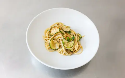 Spaghetti alla Nerano, ein cremiges Pastagericht mit gebratenen Zucchinischeiben, garniert mit frischen Kräutern, serviert auf einem weißen Teller.