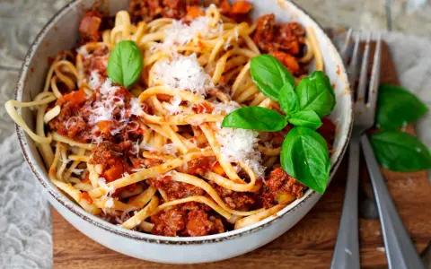 Eine Schüssel mit Linguine und einer herzhaften, **schnellen Bolognese**. Garniert mit frischem Basilikum und Parmesan.