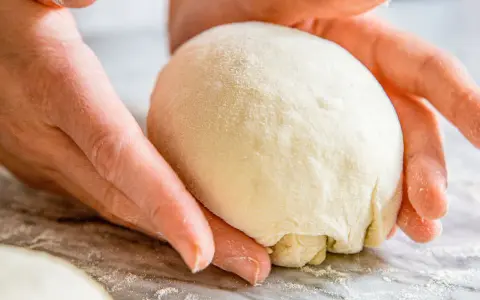 Hände formen einen Teigball, bereit zum stretch and fold pizza.