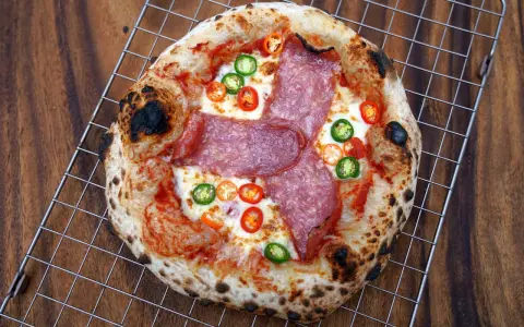 Eine scharfe Salami Pizza mit geschmolzenem Käse und bunten Chilischeiben auf einem Gitterrost.