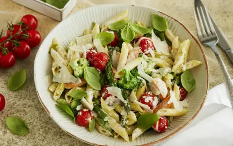 Pasta Primavera mit Penne, Brokkoli, Kirschtomaten, Spargel und Parmesan. Frisches Basilikum garniert dieses köstliche Gericht.