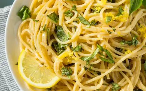 Spaghetti al limone, garniert mit frischem Basilikum und Zitronenschale, serviert mit einer Zitronenspalte.