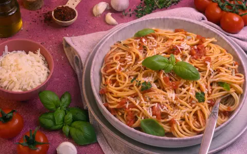 Ein Teller Spaghetti Napoli mit Tomatensauce, Basilikum und Parmesan. Daneben frische Tomaten, Knoblauch und Kräuter.