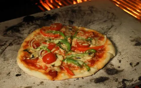 Eine köstliche Pizza mit Tomaten, Paprika und Pilzen wird auf einem Pizzastein im Ofen gebacken, wo die Flammen lodern.