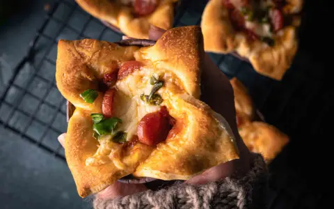 Hand hält einen herzhaften Pizza-Muffin mit geschmolzenem Käse, Wurst und grünen Paprika.