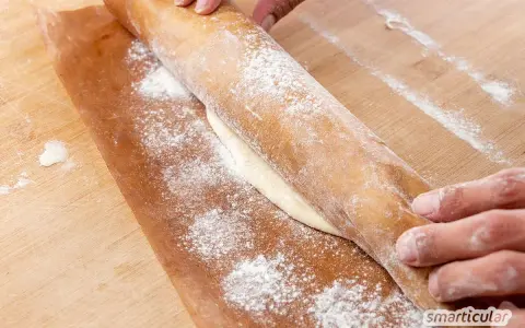 Hände rollen Teig auf Backpapier aus. Perfekt, um gegangenen Pizzateig einzufrieren und später zu verwenden.
