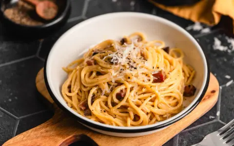 Eine Schüssel cremiger Spaghetti Carbonara, bestreut mit Parmesan und schwarzem Pfeffer, bereit zum Genießen.