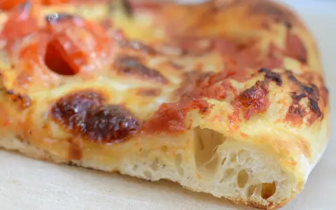 Ein Stück Pizza mit luftigem pizzateig, frisch aus dem pizzaofen. Der Teig ist goldbraun gebacken, die Tomatensoße und der Käse sind perfekt geschmolzen.