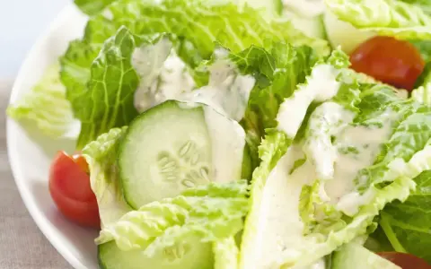 Frischer Romana Salat mit Gurkenscheiben und Tomaten, beträufelt mit cremigem Dressing.
