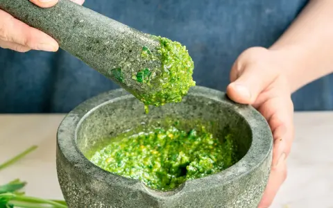 Frisches basilikum pesto wird in einem Mörser zerstoßen. Tropfen des grünen Pesto fallen vom Stößel in die Schüssel.