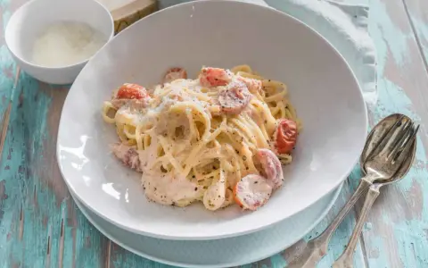 Cremige Pasta al Salmone mit Kirschtomaten und Parmesan, serviert auf einem rustikalen Holztisch.