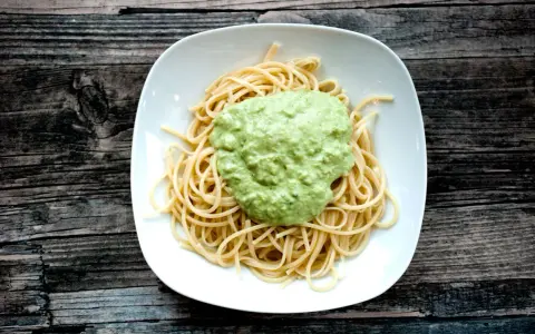 Spaghetti mit cremigem Avocado Pesto auf einem weißen Teller, serviert auf rustikalem Holz.
