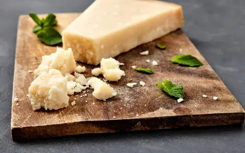 Ein Stück und zerbrochene Stücke von ist parmigiano parmesan liegen auf einem Holzbrett, garniert mit Minzblättern.