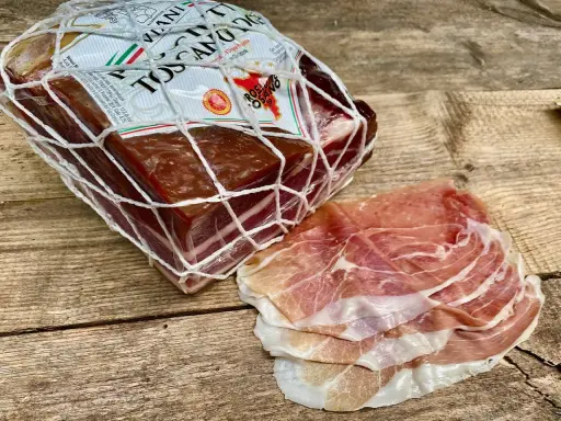 Ein Block **Prosciutto Toscano** im Netz und daneben dünn geschnittene Scheiben.