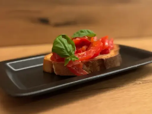 Eine Scheibe geröstetes Brot mit frischen Tomaten und Basilikum, die Haupt-Bruschetta-Zutaten, auf einem schwarzen Teller.