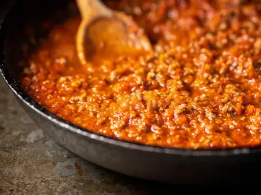 Eine Pfanne mit köstlicher, original italienischer Bolognese-Sauce, die mit einem Holzlöffel umgerührt wird.