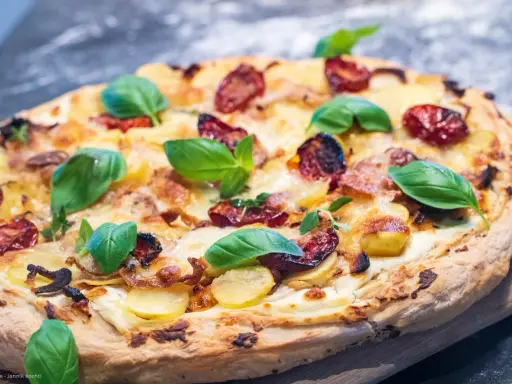 Pizza mit Sahne statt Tomatensauce, belegt mit Kartoffeln, getrockneten Tomaten und frischem Basilikum.
