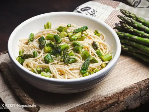 Eine Schüssel mit Spaghetti und frischem Spargel, dane liegt ein Bund grüner Spargel. Ein köstliches Gericht, das Lust auf mehr macht.