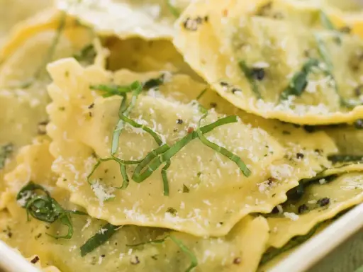 Mezzaluna pasta, gefüllt und mit Kräutern und Parmesan bestreut, liegt appetitlich in einer Schale.