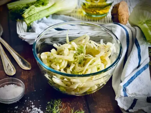 Frischer Fenchel Salat in einer Glasschüssel, garniert mit Dill. Daneben liegen Löffel und eine kleine Schale mit Salz.